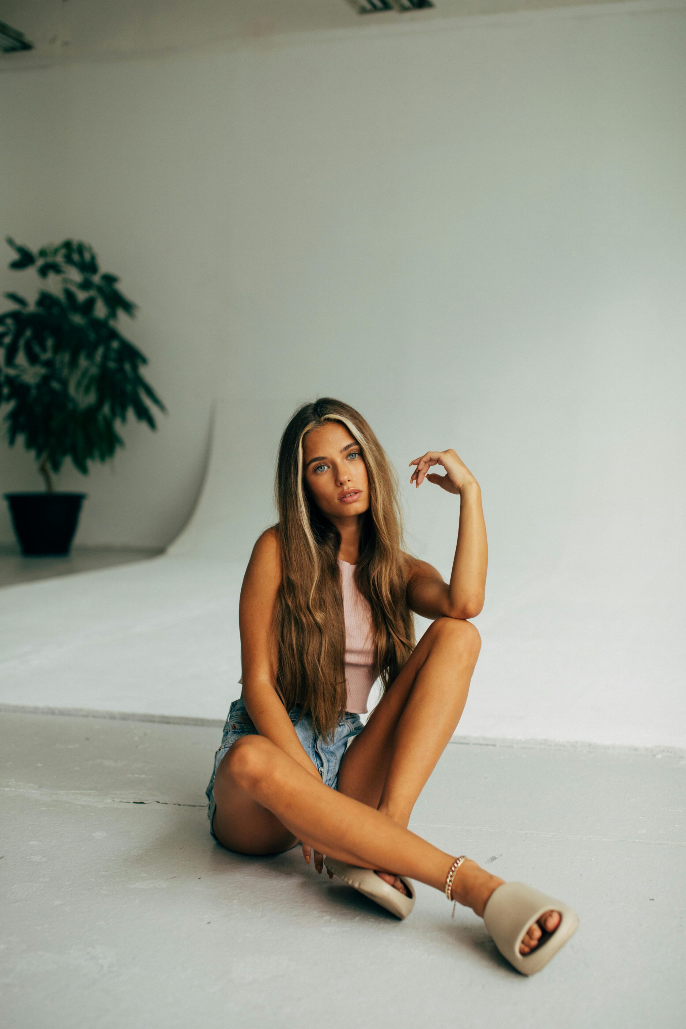 A fashionable young woman with long hair poses in a modern, minimalist studio setting.